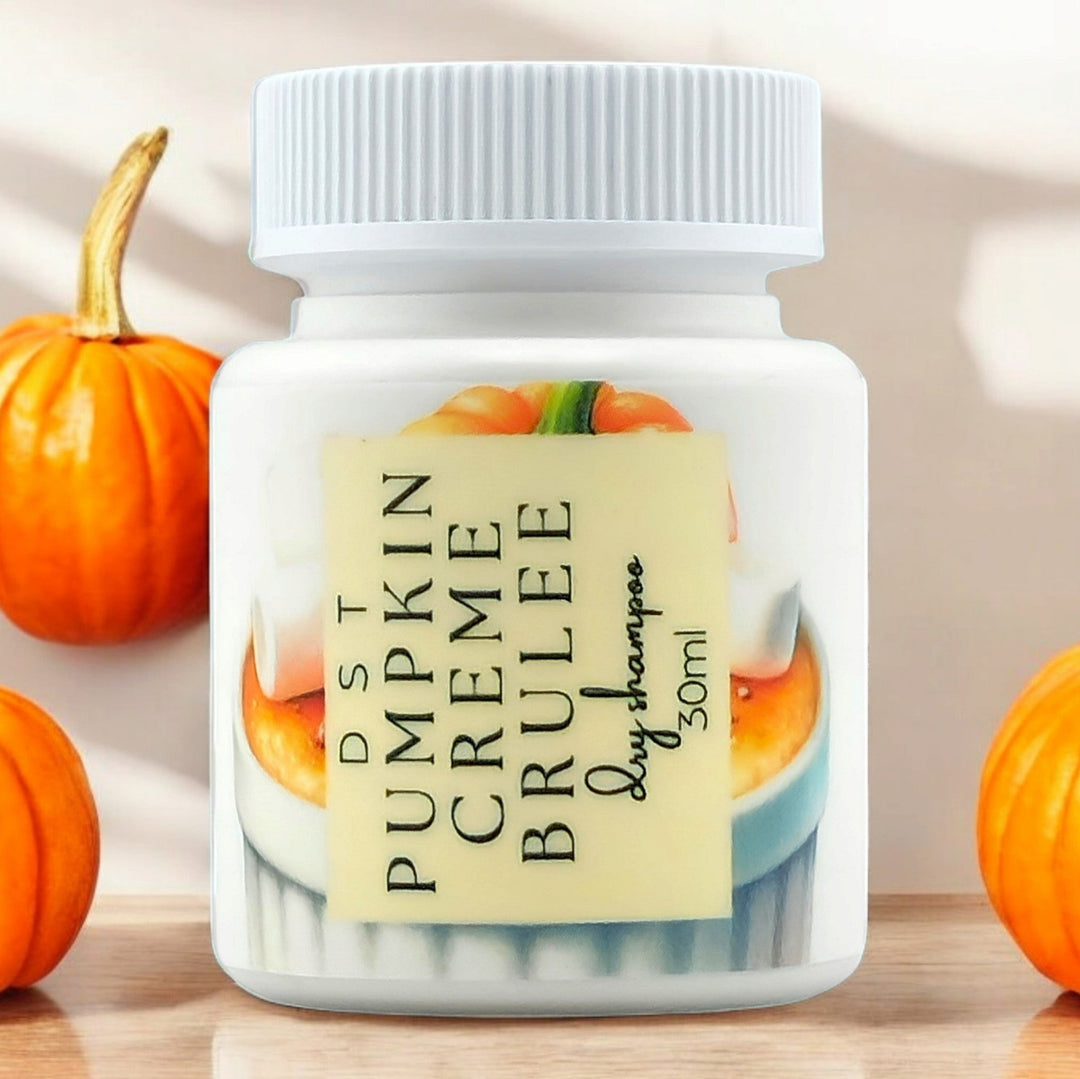 30ml bottle of Pumpkin Creme Brulée scented Dry Shampoo powder sitting on a wood countertop with pumpkins in the ivory backdrop. 