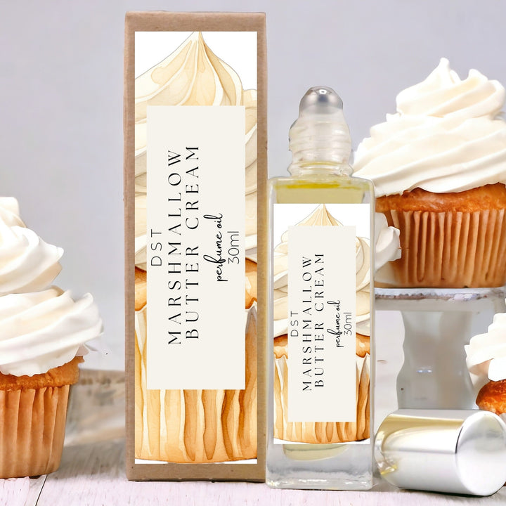 30ml bottle of Marshmallow Butter Cream Perfume Oil and the box it is packaged in against a grey background with several cupcakes topped with Marshmallow Frosting. 