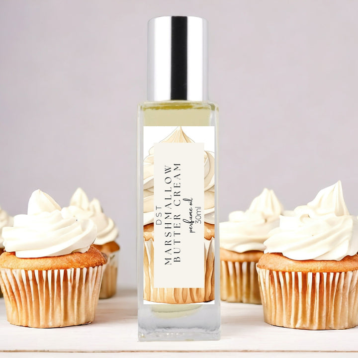 30ml bottle of Marshmallow Butter Cream Perfume Oil against a grey background with several cupcakes topped with Marshmallow Frosting. 