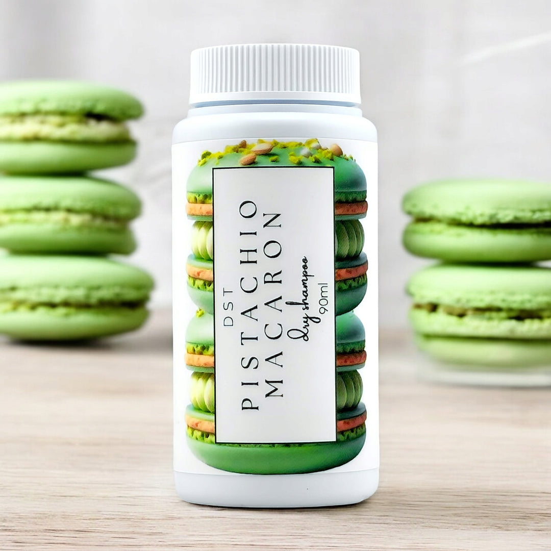 90ml bottle of Pistachio Macaron scented Dry Shampoo powder sitting on a wood countertop with green French Macarons in the background.