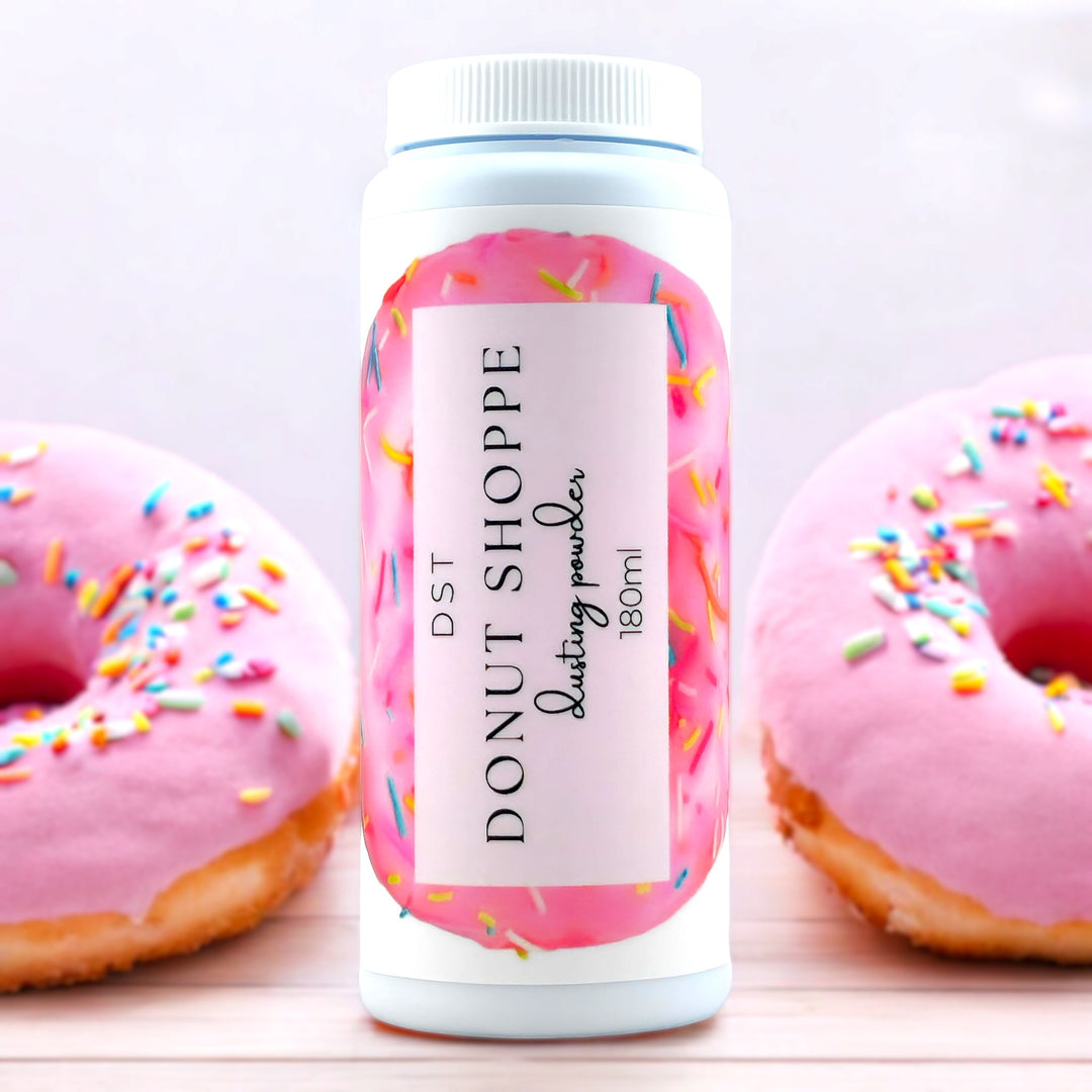 180ml bottle of Donut Shoppe scented body powder against a light pink background with 2 pink donuts covered with rainbow sprinkles.