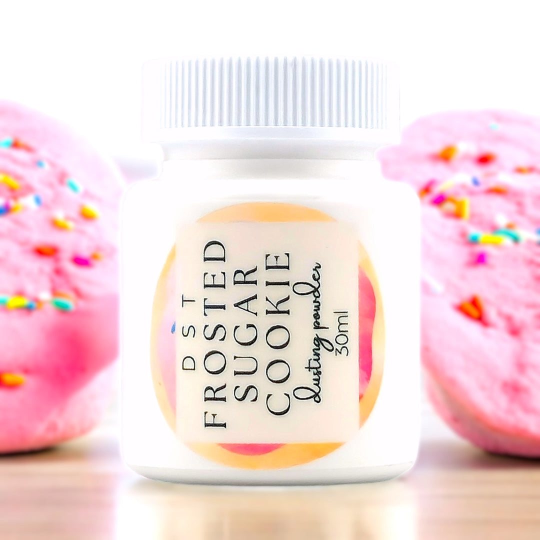 30ml bottle of Frosted Sugar Cookie scented body powder against a white background with pink Frosted Sugar Cookies.