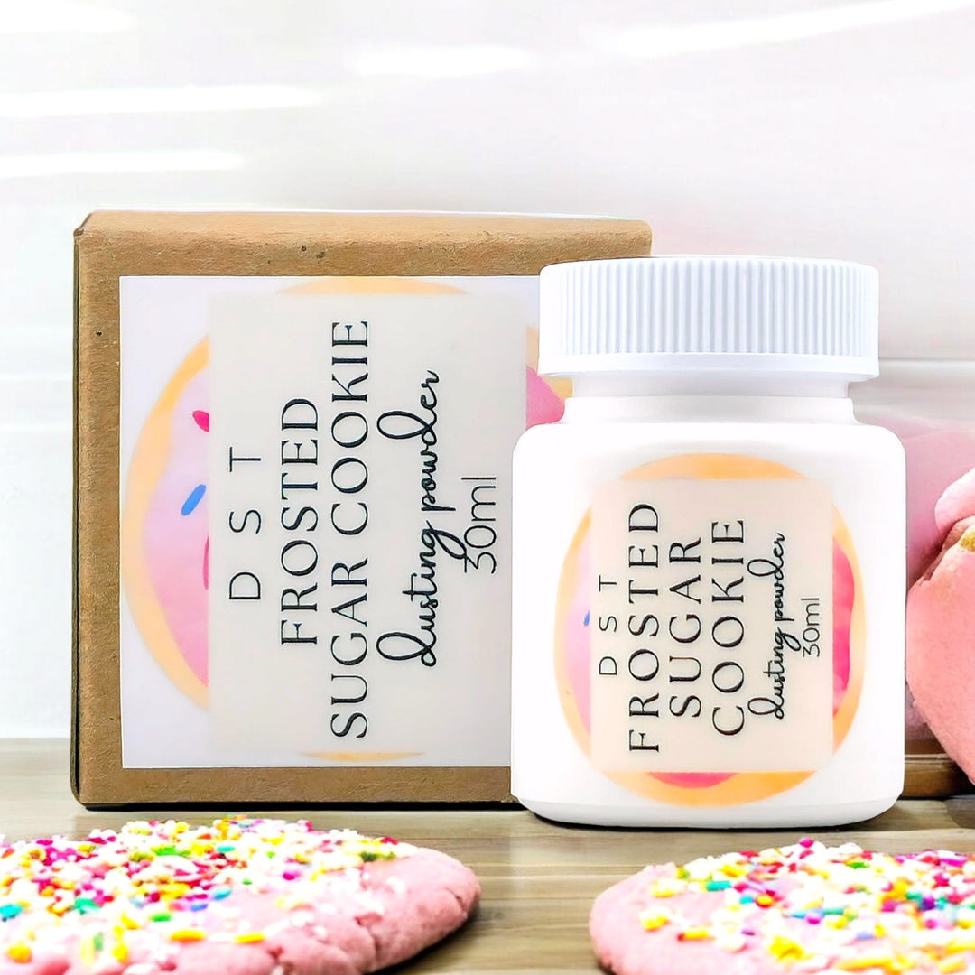 30ml bottle of Frosted Sugar Cookie scented body powder and the box it is packaged in against a white background with pink Frosted Sugar Cookies.