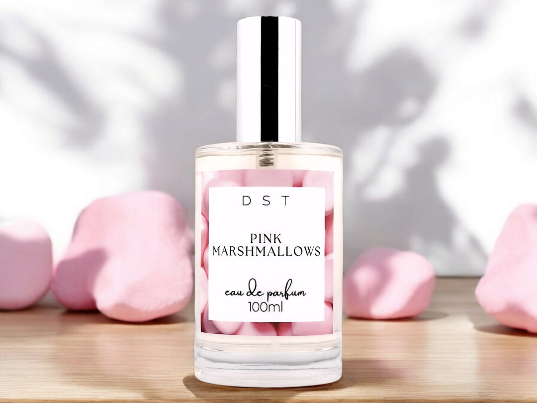 100ml bottle of Pink Marshmallows Eau de Parfum spray sitting on a wood countertop with fluffy pink marshmallows against a white shadowy background.