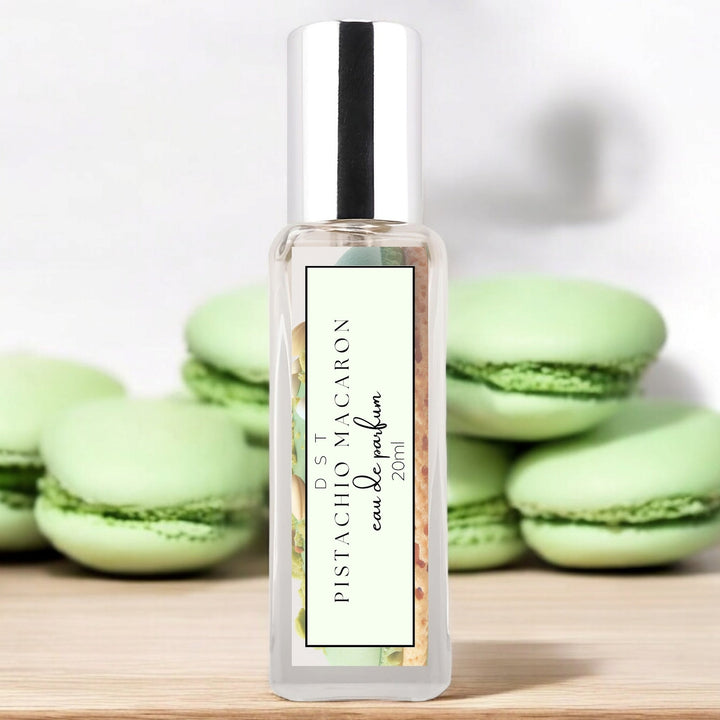 20ml bottle of Pistachio Macaroon Eau de Parfum sitting on wood counter top with white background and green macarons surrounding the bottle.