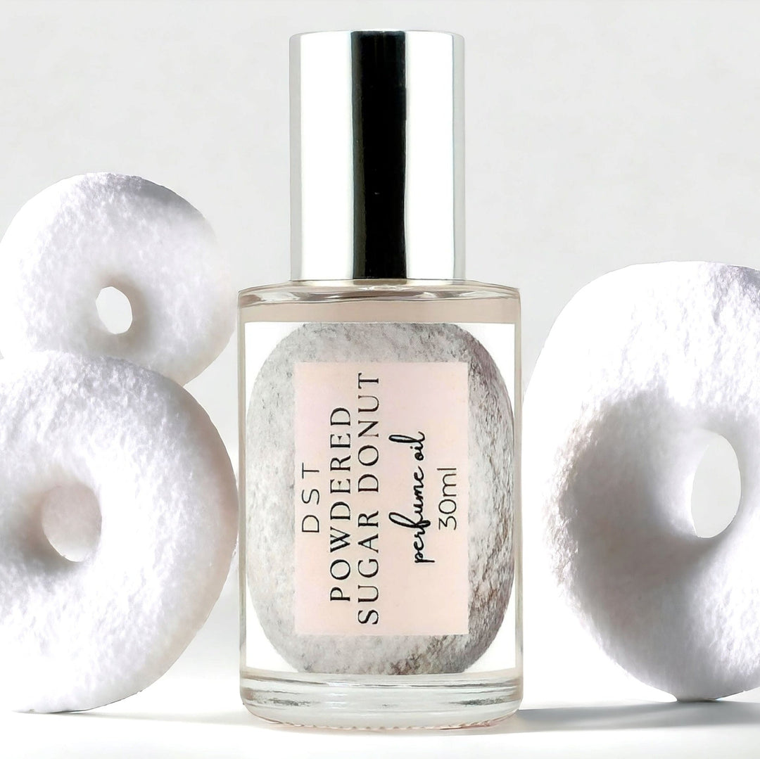 30ml bottle of Powdered sugar donut perfume oil against a grey background with stacked powderedsugar donuts. 