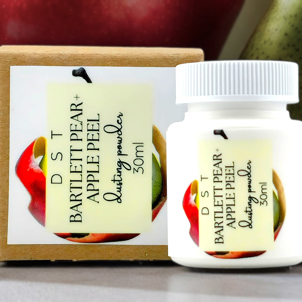 30ml bottle of Bartlet Pear and Apple Peel scented body powder and the box it is packaged in surrounded by light green background and red Apples and green pears. 