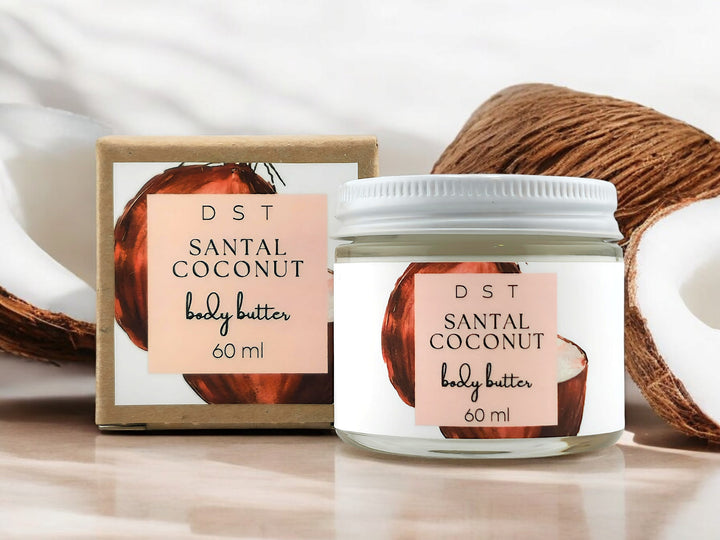 120ml jar of Santal Coconut scented body butter and the box it is packaged in sitting on wood countertop coconuts in the white shadowy background.