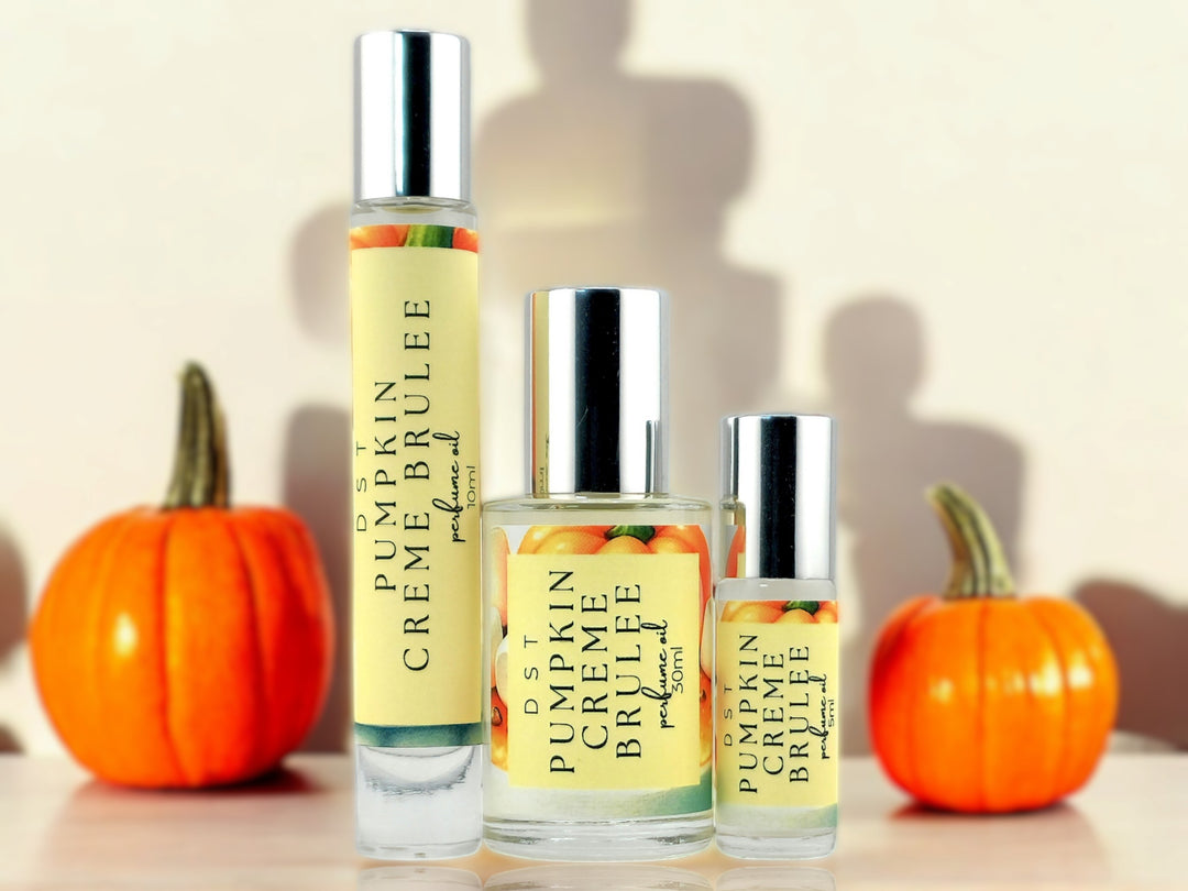 5, 10 and 30ml bottles of Pumpkin Creme Brulee perfume oil sitting on wood countertop with 2 pumpkins and cream-colored shadowy background.