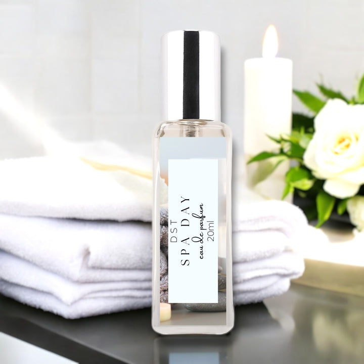 20 milliliter bottle of spa day perfume sitting on a gray countertop with white towels, a white lip candle, and a bouquet of white roses.