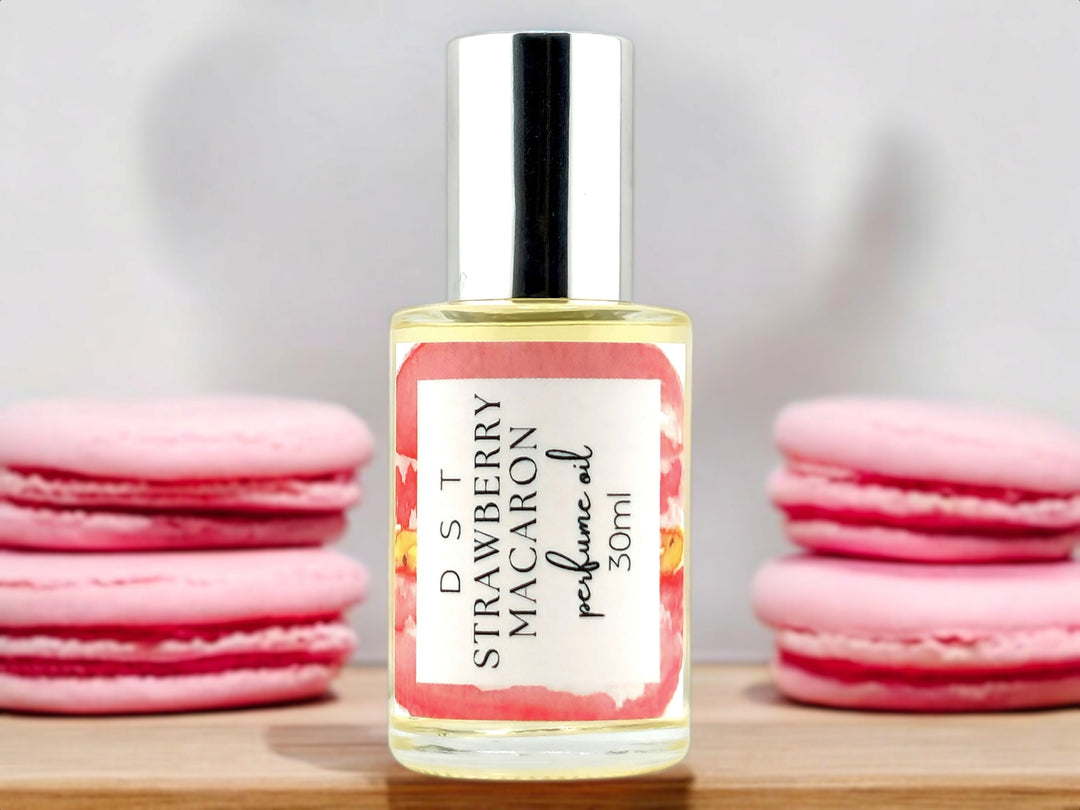 30ml bottle of Strawberry macaron perfume oil sitting on wood countertop with pink macarons stacked against a white shadowy background.