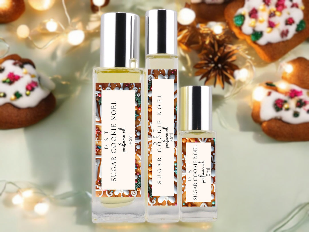 5, 10 and 30ml bottles of Sugar Cookie Noel Perfume Oil sitting on a glass surface with decorated gingerbread cookies and twinkling fairy lights against pastel green background.