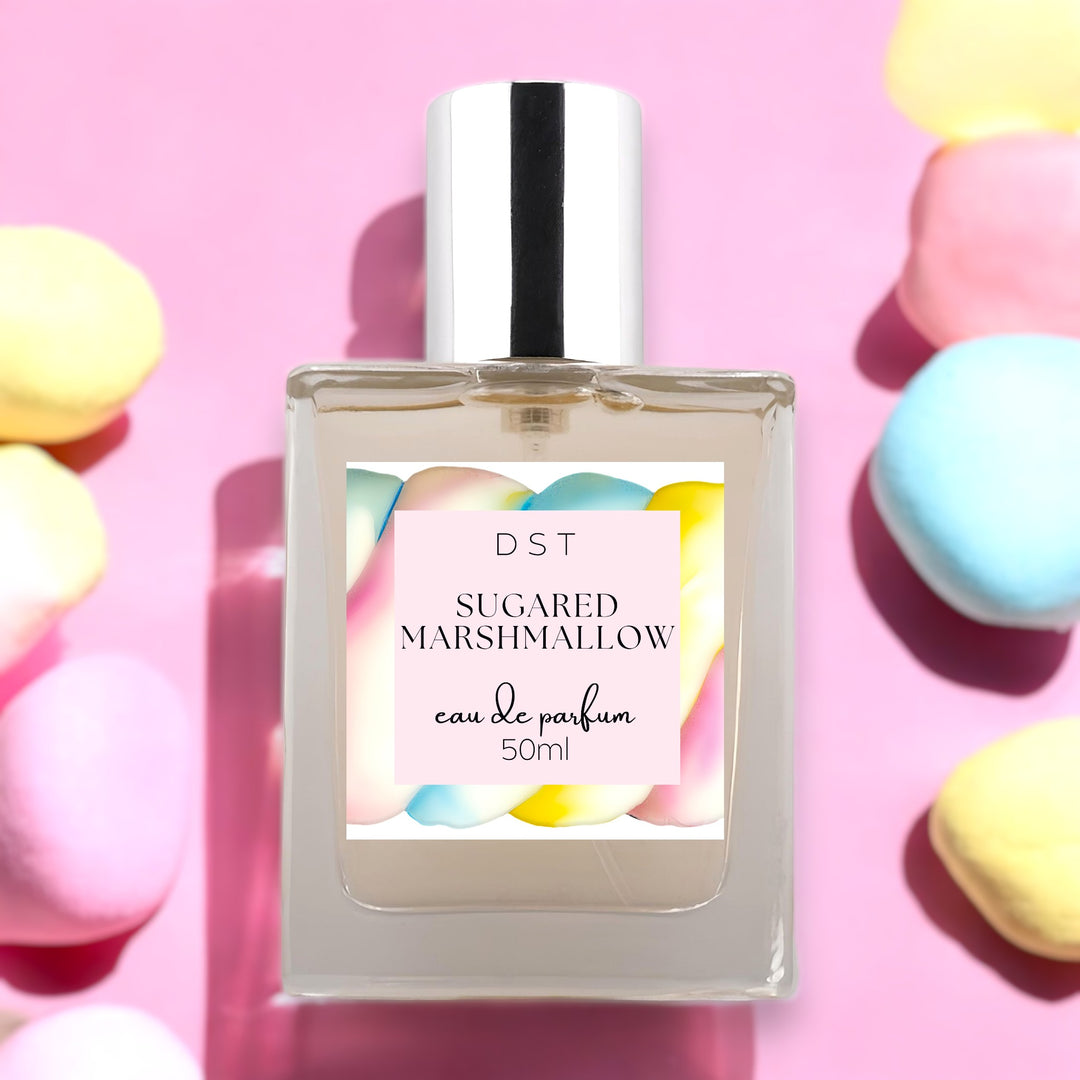 Fifty milliliter bottle of sugared marshmallow perfume against a pastel pink background with pastel colored marshmallows.