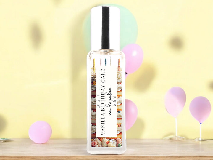 20ml bottle of Vanilla birthday Cake Eau de Parfum spray sitting on a wood countertop with pastel pink and blue balloons against a pastel yellow background.