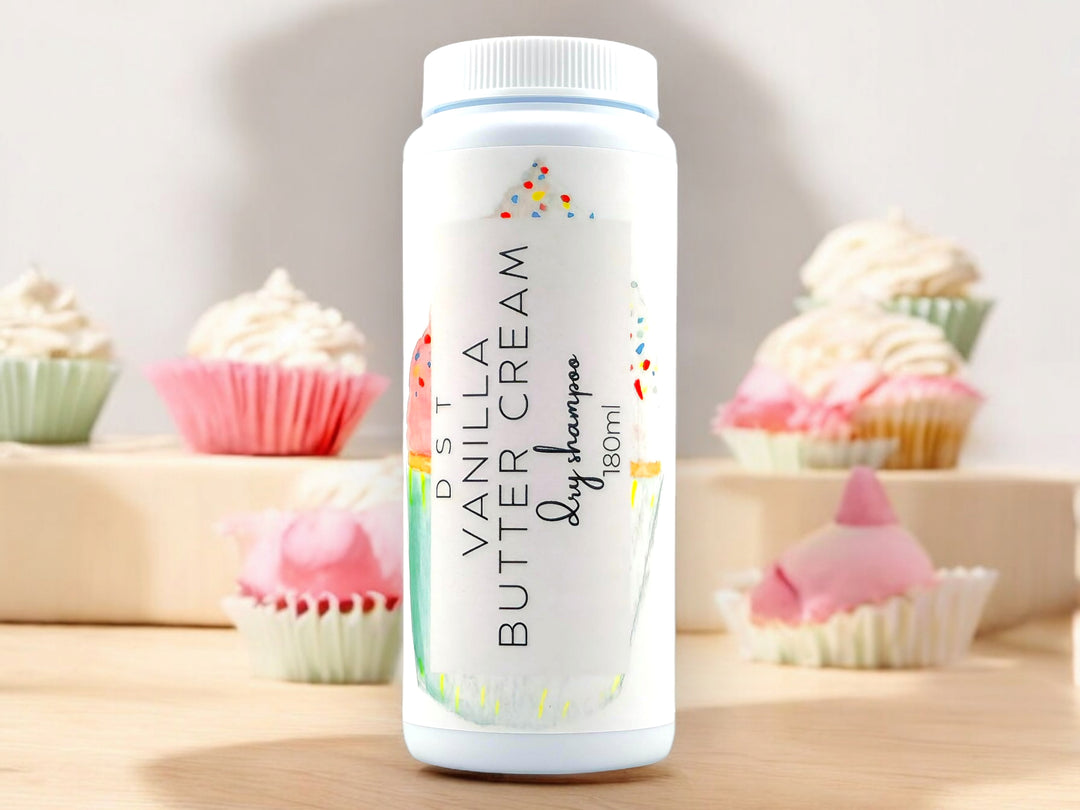 180ml bottle of Vanilla Butter Cream scented Dry Shampoo powder sitting on wood countertop with 6 colorful cupcakes set against white background.