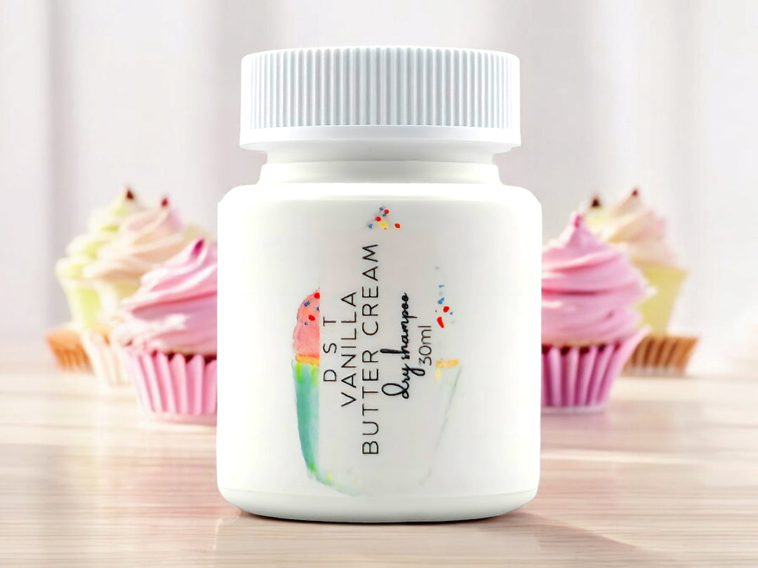 30ml bottle of Vanilla Butter Cream scented Dry Shampoo powder sitting on wood countertop with 6 colorful cupcakes set against white background.