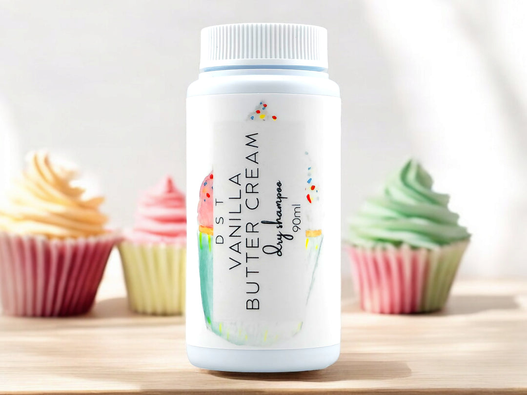 90ml bottle of Vanilla Butter Cream scented Dry Shampoo powder sitting on wood countertop with 3 colorful cupcakes set against white background.