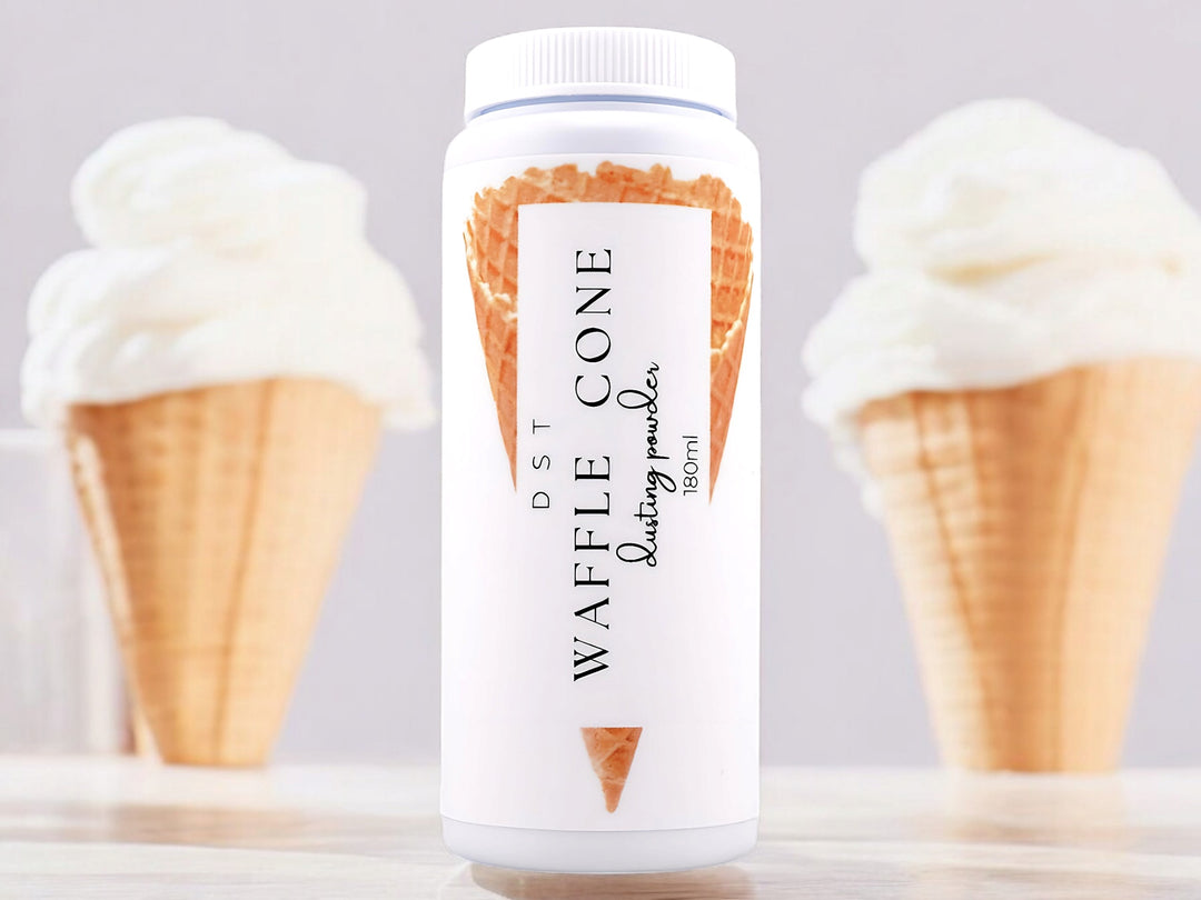 A 180ml bottle of waffle cone scented body powder sitting on a wood countertop with 2 vanilla ice cream cones against a white background.