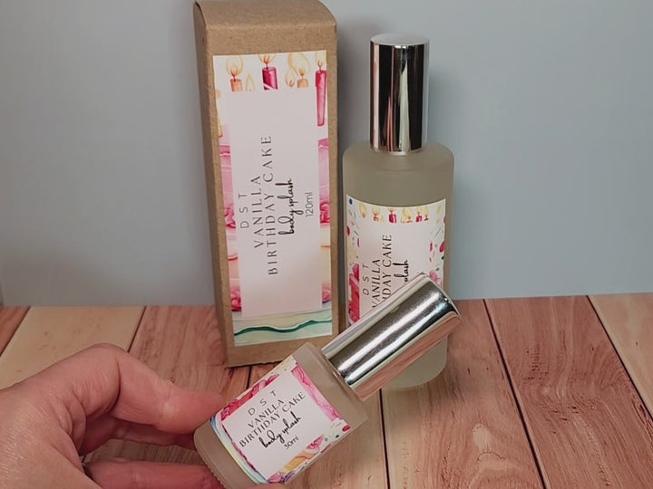 30 and 120ml bottles of Vanilla birthday cake body splash and the box it is packaged in sitting on wood countertop with pastel blue background.