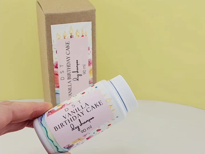 90ml bottle of Vanilla Birthday Cake scented dry shampoo sitting on a white countertop, followed by Model demonstrating how to use dry shampoo powder. She sprinkles it at the base of the scalp and gently rubs it in with her fingertips.