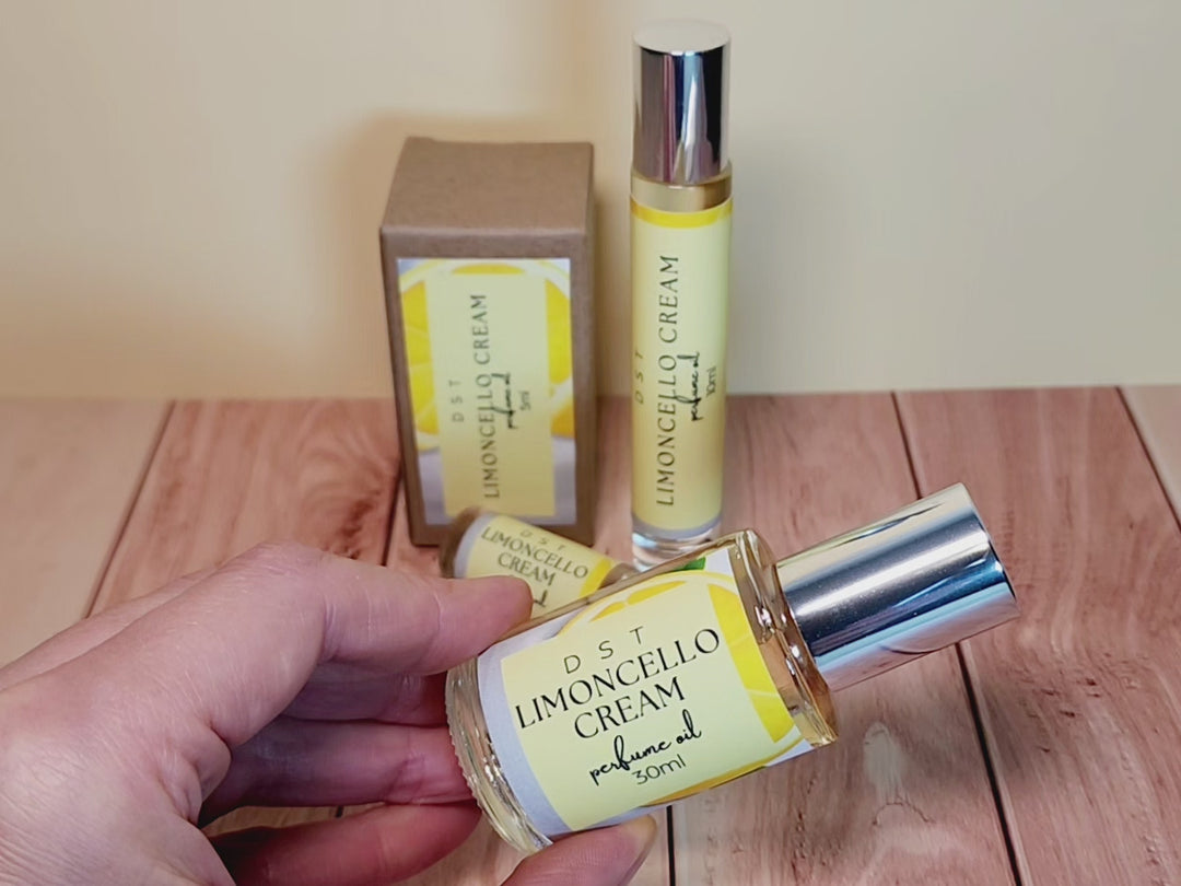 5, 10, and 30ml bottles of Limoncello Cream Perfume Oil and the box that it is packaged in sitting on wood countertop with pale yellow background.