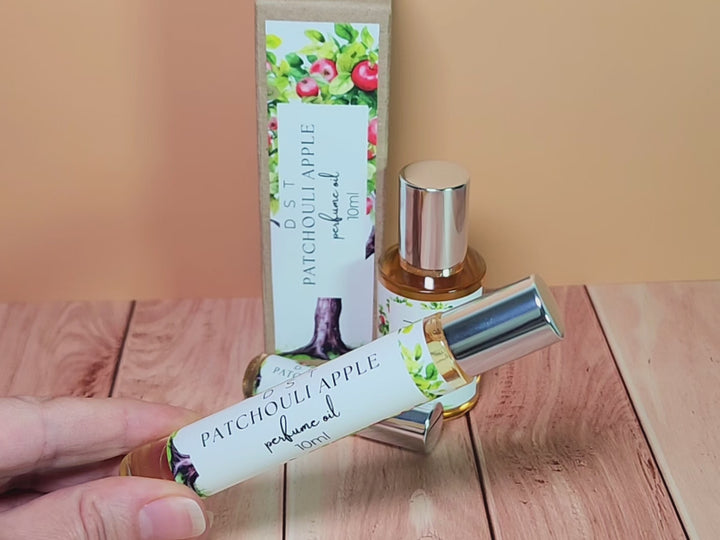 5, 10, and 30ml bottles of Patchouli Apple perfume oil and the box it is packaged in sitting on wood countertop with tan background.