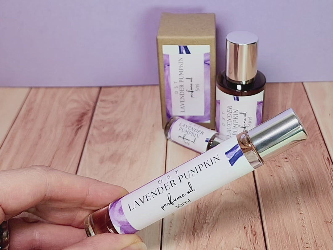 5, 10, and 30ml bottles of Lavender Pumpkin perfume oil and the box it is packaged in sitting on wood counter top with lavender colored background.