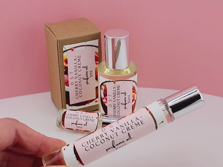 5, 10, and 30ml bottles of Cherry Vanilla and Coconut Cream perfume oil sitting on white countertop with paetel pink background.