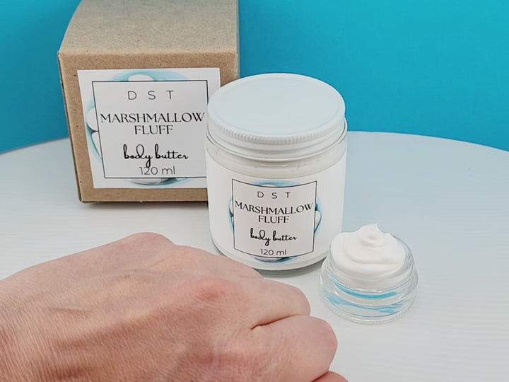 120ml jar of Marshmallow Fluff scented Body Butter and the box it is packaged in. Model shown rubbing a small amount of body butter on her hand to show consistency of product.