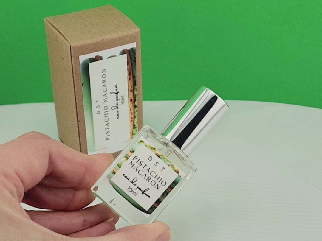 10ml bottle of Pistachio Macaron Eau de Parfum and the box it is packaged in sitting on white countertop against green background. 