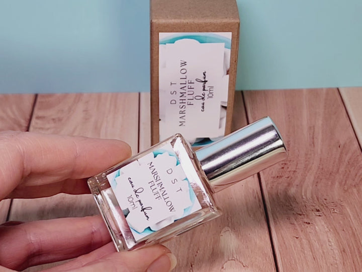 10ml bottle of Marshmallow Fluff Eau de Parfum and the box it is packaged in sitting on wood counter top with light blue background.