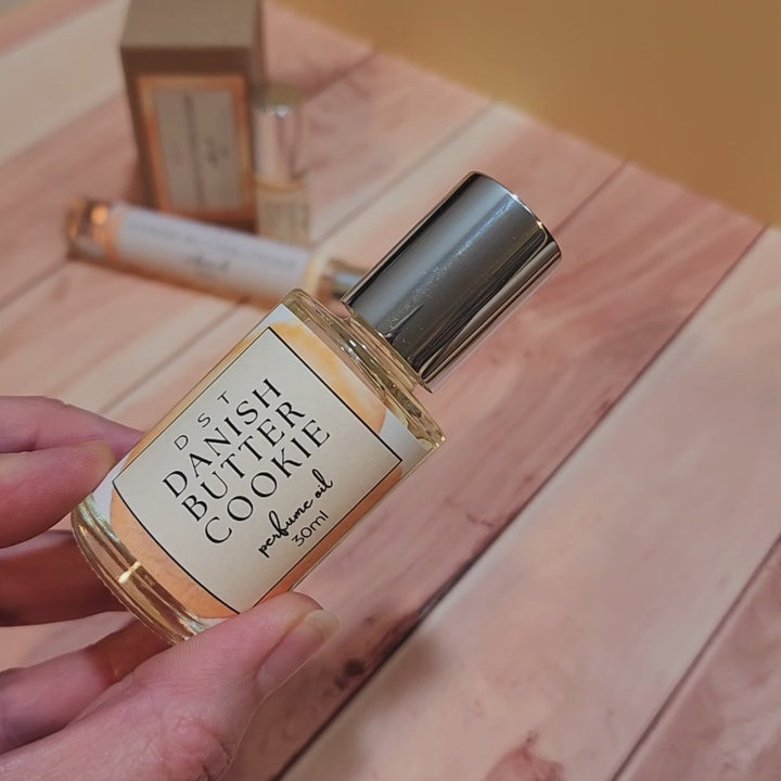 5, 10, and 30ML bottle of Danish Butter Cookie perfume oil sitting on a wood countertop against a tan background.