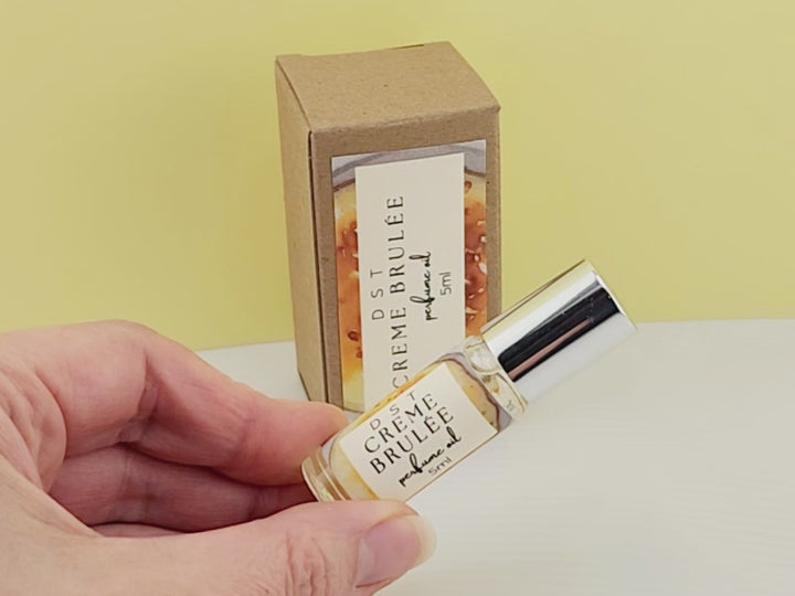 5ml bottle of Creme Brulee perfume oil and the box it is packaged in sitting on a white countertop with yellow background.