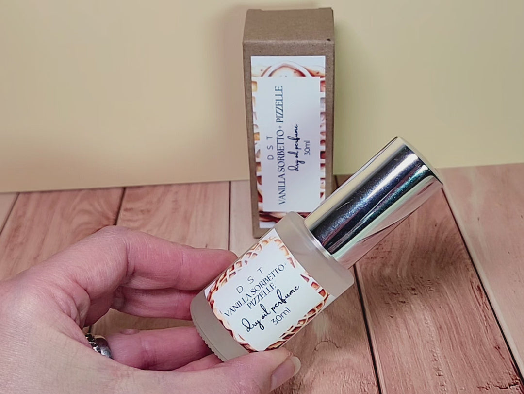 30ML bottle of Vanilla Sorbetto and Puzzelle Dry Oil Perfume Spray and the box it is packaged in on a wood counter top with cream background. 