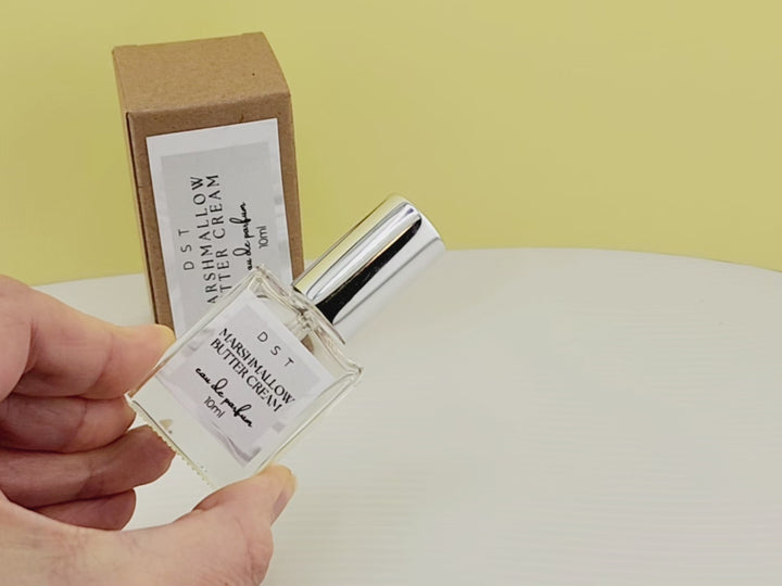 10ml bottle of Marshmallow Butter Cream Eau de Parfum and the box it is packaged in sitting on a white countertop with pastel yellow background. 