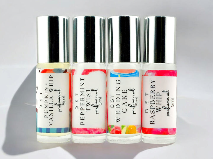 4 5ml deluxe perfume oil roll-on samples against a white shadowy background. The following scents are shown as representative samples of the scents I offer: Pumpkin and Vanilla Whip, Peppermint Twist, Wedding Cake, Raspberry Whip.